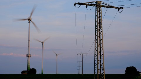 Das Farbfoto zeigt Strommasten und Windräder vor einem blauen Himmel.