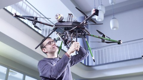 Auf dem Bild ist ein Mann zu sehen, der eine große Drohne in der Hand hält