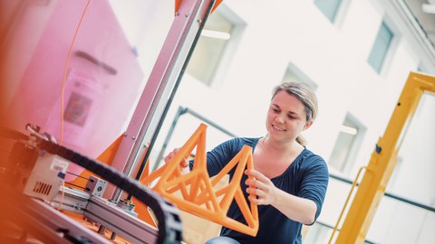 Auf dem Bild ist eine Frau zu sehen, die ein Brückenmodell aus Kunststoff in der Hand hält