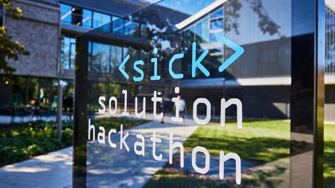 Auf einer Fensterscheibe sieht man die Aufschrift Sick Solution Hackathon. Im Hintergrund ist ein neu gebautes Gebäude zu sehen.