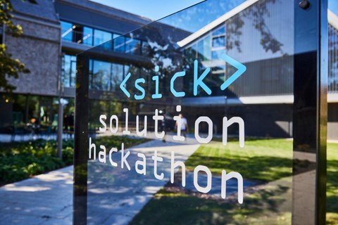 Auf einer Fensterscheibe sieht man die Aufschrift Sick Solution Hackathon. Im Hintergrund ist ein neu gebautes Gebäude zu sehen.