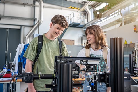  Zwei Schüler:innen der Junior-Ingenieur-Akademie während der Blockwoche auf dem Campus der TU Dresden an einem Prüfstand zur Untersuchung von Wasserstoffblasen. 