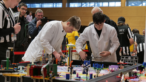 Zwei Schüler in weißen Kitteln an Robotik-Spielfeld