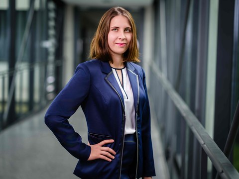 Junge Frau mit schulterlangen braunen Haaren in blauen Blazer posiert mit eingestützter Hand in der Hüfte