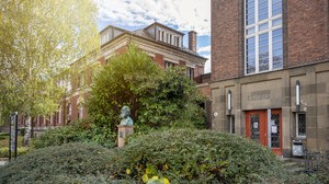 Das Foto zeigt den Eingang des Zeuner-Baus der TU Dresden. Im Vordergrund erkennt man eine Statue und einige Büsche.