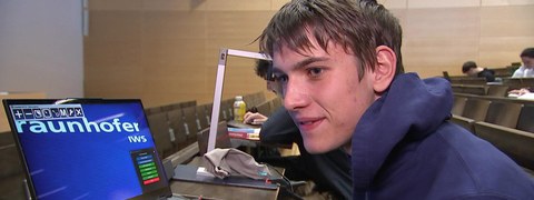 Student sitzt in Hörsaal mit seinem Laptop, auf dem ein vergrößertes Bild zu sehen ist.
