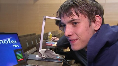 Student sitzt in Hörsaal mit seinem Laptop, auf dem ein vergrößertes Bild zu sehen ist.