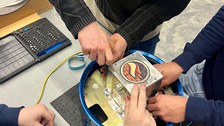 Gemeinsam montiert das SHAMA-Team das Elektronikgehäuse des Experiments während der Integrationsphase. 