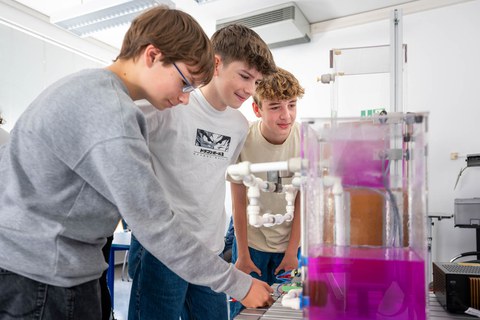 Auf dem Bild sind 3 Schüler zu sehen, die vor einem chemischen Gemisch stehen