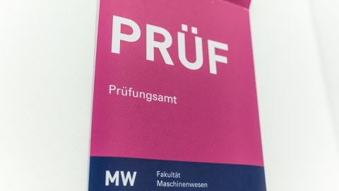 Foto:  Hinweisschild mit PRÜF (in sehr großer Schrift), darunter steht Prüfungsamt, am unteren Rand des Schildes steht MW Fakultät Maschinenwesen