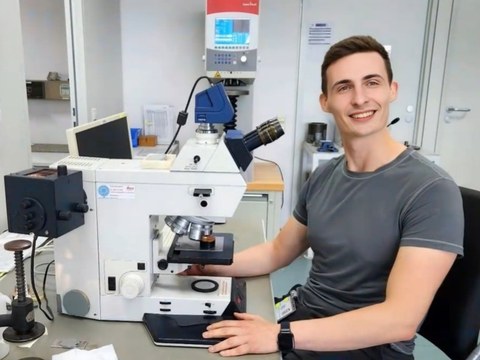 Junger Mann sitzt an Mikroskop in Labor