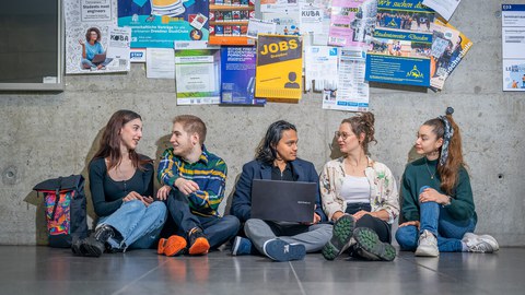 Auf dem Bild sind Studierende zu sehen, die auf dem Boden sitzen und lernen