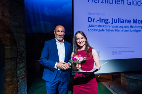 Junge Frau mit braunen Haaren in rotem Kleid mit Blumenstrauß neben Mann in blauen Anzug