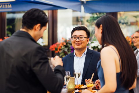Gruppe von Absolventen und Absolventinnen unterhält sich - zentriert ein junger Asiate mit Brille und Anzug
