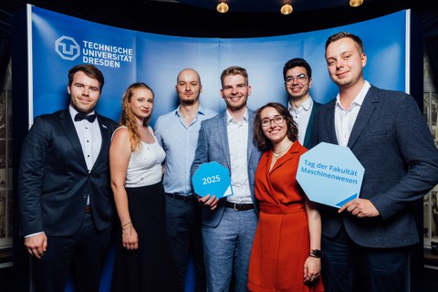 Gruppe von Absolventinnen und Absolventen posiert vor Fotowand