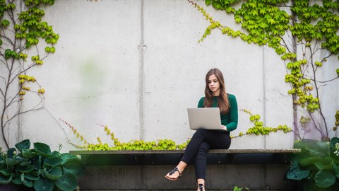 Das Bild zeigt eine Studentin mit einem Notebook. Sie sitzt auf einer Bank vor einer mit Grünpflanzen bewachsenen Wand.