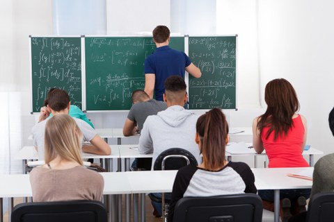 Das Bild zeigt eine klassische Unterrichtssituation in einer Kleingruppe. Ein Tutor schreibt an der Tafel. Es handelt sich um Mathematikunterricht.