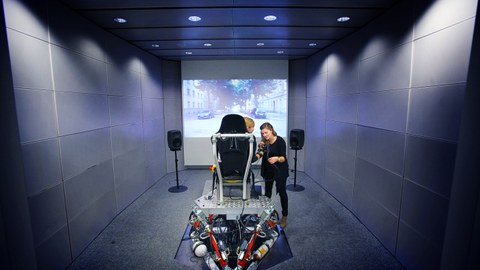 Das Foto zeigt den Blick in das Multimodale Messlabor der Fakultät Elektrotechnik und Informationstechnik. Im Zentrum des Bildes sieht man zwei Personen. Eine Person sitzt aufdem Versuchsaufbau, die zwei unterstützt und erklärt die Handhabung.