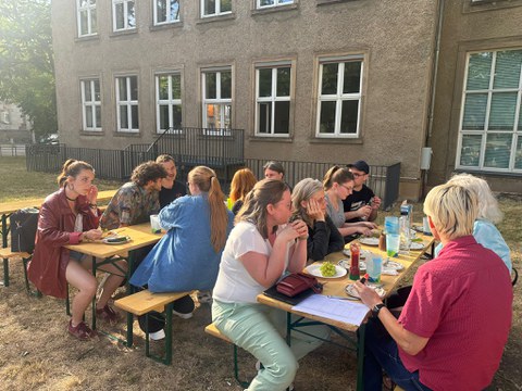 eine Gruppe Personen die sich an Biertischen beim Essen unterhält