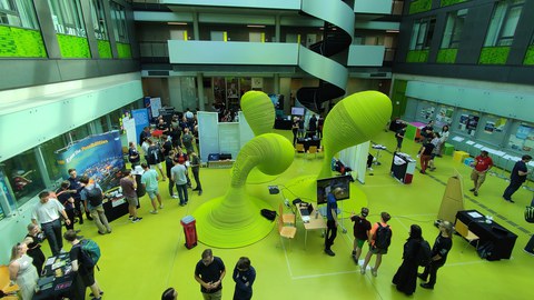 Blick ins Foyer des Andreas-Pfitzmann-Baus, Menschen informieren sich an Ständen und sind im Gespräch.