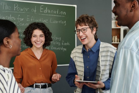 Gruppe von Personen, die in einem Klassenzimmer mit einer Kreidetafel im Hintergrund über Grundsätze für effektives Lernen diskutieren. Die Gruppenmitglieder lächeln und sind in ein Gespräch vertieft.