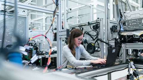 Frau sitzt an einem Laptop an einem Versuchsstand