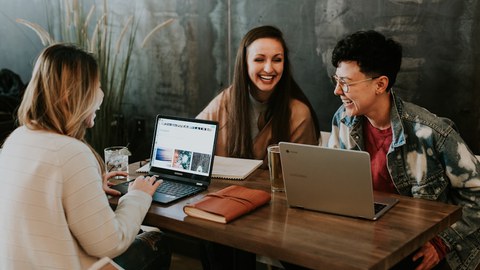 Drei Personen sitzen mit aufgeklappten Laptop an einem Tisch.