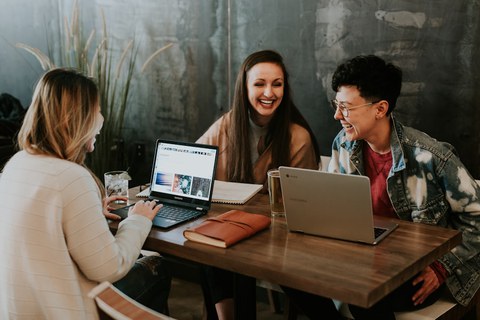Drei Personen sitzen mit aufgeklappten Laptop an einem Tisch.