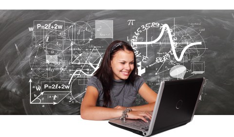 Das Bild zeigt eine junge, lachende Frau vor einem Laptop und im Hintergrund eine Tafel mit mathematischen Darstellungen in Kreide geschrieben.