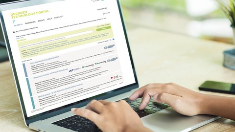 In the photo you can see the hands of a person on a laptop keyboard. The person is searching in the DRESDEN Technology Portal.