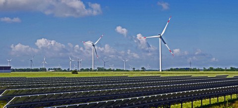 On the photo you can see a landscape with a solar park consisting of wind turbines and solar panels.