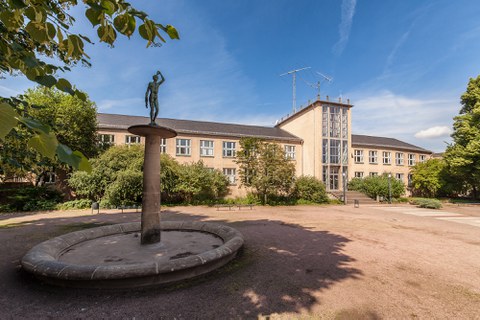 Das Foto zeigt den Blick auf den Barkhausen-Bau der TU Dresden. Im Vordergrund links sieht man den Brunnen, der auf der Freifläche vor dem Barkhausen-Bau steht.