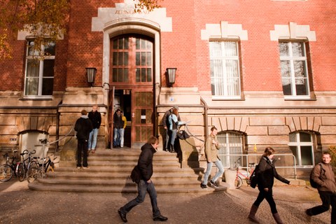Auf dem Foto sieht man den Haupteingang des Zeuner-Baus. Studierende verlassen das Gebäude. 