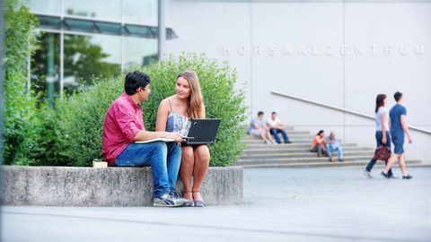 Zwei Studierende sitzen vor dem Hörsaalzentrum der TU Dresden und unterhalten sich.