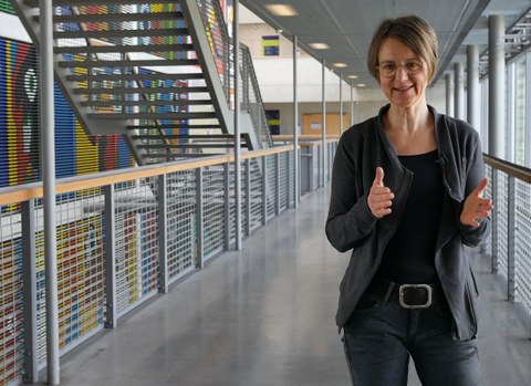 The picture shows Dr. Sandra Buchmüller in the main lecture hall. In the background, you can see a stairway and a colorful wall painting.