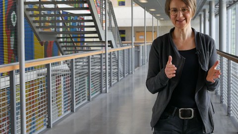 The picture shows Dr. Sandra Buchmüller in the main lecture hall. In the background, you can see a stairway and a colorful wall painting.