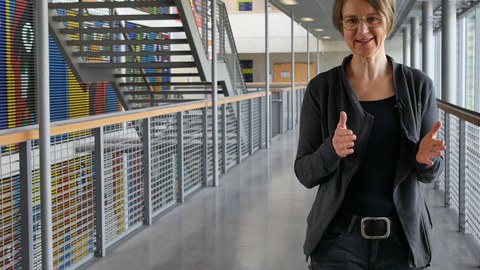 The picture shows Dr. Sandra Buchmüller in the main lecture hall. In the background, you can see a stairway and a colorful wall painting.