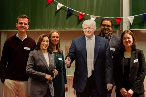 Group picture of the speakers with life-size cardboard cut-outs of Kamala Harris and Donald Trump.