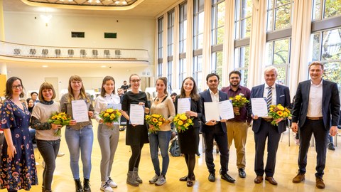 Auf dem Bild sieht man die Preisträger:innen des Preis Internationalisierung 2022 bei der Preisverleihung im Dülfersaal der TU Dresden mit Urkunden und Blumensträußen.