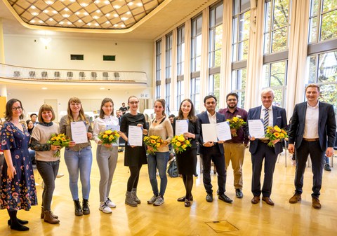 Auf dem Bild sieht man die Preisträger:innen des Preis Internationalisierung 2022 bei der Preisverleihung im Dülfersaal der TU Dresden mit Urkunden und Blumensträußen.