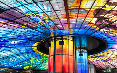 Farbenprächtige Glasskulptur in einem Gebäude. Die Skulptur nimmt den ganzen Raum ein. 