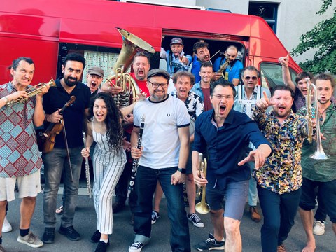 Gruppenfoto der Banda Comunale vor einem roten Transporter. Viele Personen halten Instrumente in der Hand. Es herrscht eine ausgelassene Stimmung.