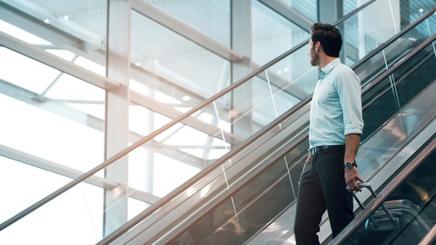 Foto einer Person mit Koffer auf einer Treppe in einer großen Glashalle