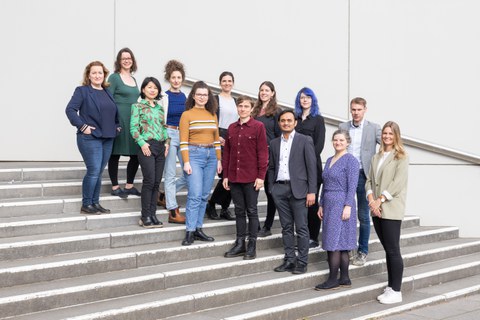 Gruppenfoto mit dreizehn Personen, die in zwei Reihen auf einer Treppe stehen