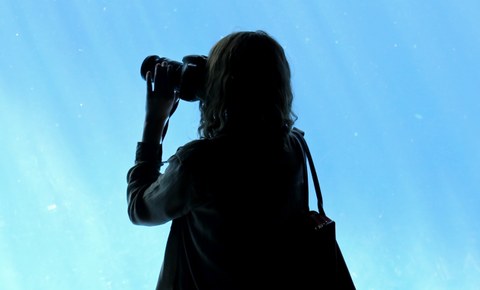 Frauen-Silhouette mit Fernglas vor blauem Himmel