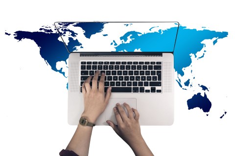 Draufsicht eines Laptops mit Händen auf der Tastatur. Der Desktop zeigt den Ausschnitt einer eurozentristischen Weltkarte. Dieser Ausschnitt wird im Hintergrund, um den Laptop herum, weitergeführt.