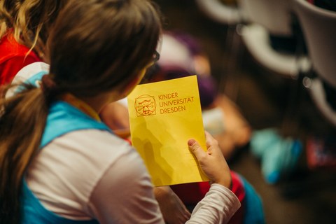 Ein Mädchen hält das Schreibheft der Kinder-Uni in der Hand.