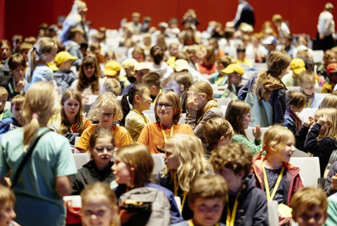 Viele Kinder sitzen in Stuhlreihen.