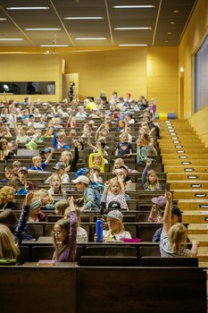 Viele Kinder sitzen in einem Hörsaal und melden sich.
