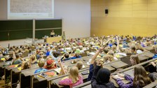 Viele Kinder sitzen in einem Hörsaal und melden sich. Dieses Bild zeigt die Kinder von hinten.